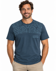A man wearing a dark blue short-sleeve t-shirt with a subtle tribal pattern across the chest and 'AUSTRALIA NEW ZEALAND' text on the lower right chest, paired with khaki pants, against a plain white background.