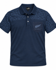 A navy blue short-sleeve polo shirt with a subtle tonal tribal pattern on the shoulders and sleeves, featuring a chest pocket with a silver fern logo and 'NEW ZEALAND' text, shown on a plain white background.