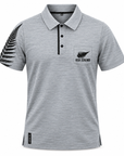 A heather gray short-sleeve polo shirt with a black fern leaf graphic on the right sleeve and a black fern leaf logo with 'NEW ZEALAND' text on the left chest pocket. The shirt features a three-button placket and is shown against a plain white background.