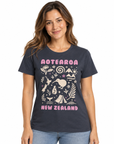 A woman wearing a dark navy graphic t-shirt with 'AOTEAROA NEW ZEALAND' and New Zealand-themed illustrations in pink and cream, paired with light blue jeans, against a plain white background.