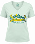 A pale mint green V-neck t-shirt featuring a retro-style graphic of New Zealand with the text 'Aotearoa NEW ZEALAND' and coordinates. The graphic includes yellow flowers, green mountains, a yellow sun, and an illustration of a hiker.