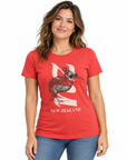 A woman wearing a red short-sleeve graphic t-shirt with a kiwi bird and New Zealand map design, paired with dark blue jeans, against a plain white background.