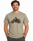 A man wearing a light khaki t-shirt with a vintage motorcycle graphic on the chest, paired with dark gray pants, against a plain white background.