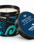 A tin candle shown open with the lid leaning beside it on a white studio background. The candle container has a black rim and a decorative label with blue, teal, black, and tan abstract patterns.