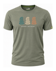 An olive green short-sleeve t-shirt with a graphic of three New Zealand Moko statues in teal, beige, and orange, with the text 'AOTEAROA - NEW ZEALAND' printed below. The brand 'Well-Tuned' is visible on the inner neck label and as a small yellow logo on the sleeve.