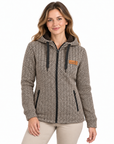 A woman wearing a zip-front hooded jacket with a beige and black herringbone pattern, black drawstrings, and a small tan brand patch on the left chest, photographed against a plain white studio background.