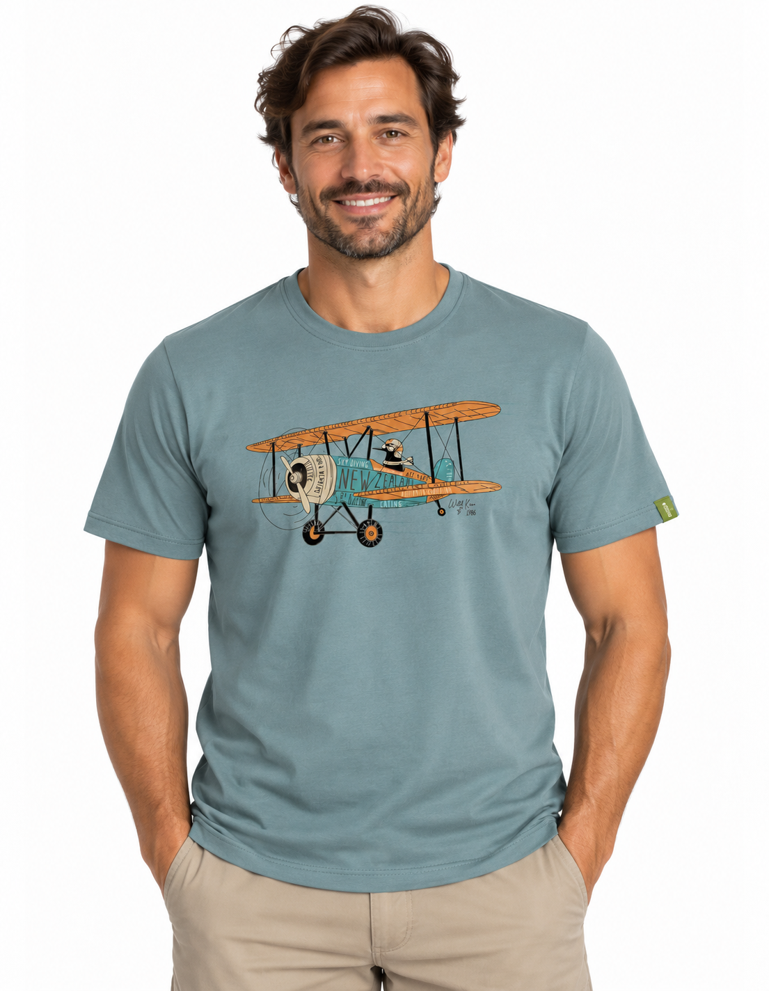 A man wearing a slate blue crewneck t-shirt with a vintage biplane graphic on the chest, paired with khaki pants, against a plain white background.