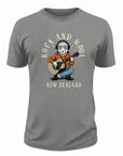 A gray short-sleeve crewneck t-shirt featuring a cartoon graphic of a sheep wearing sunglasses, an orange hoodie, and blue jeans while playing an acoustic guitar. The text 'ROCK AND WOOL' is arched above the sheep, and '- NEW ZEALAND -' is printed below.