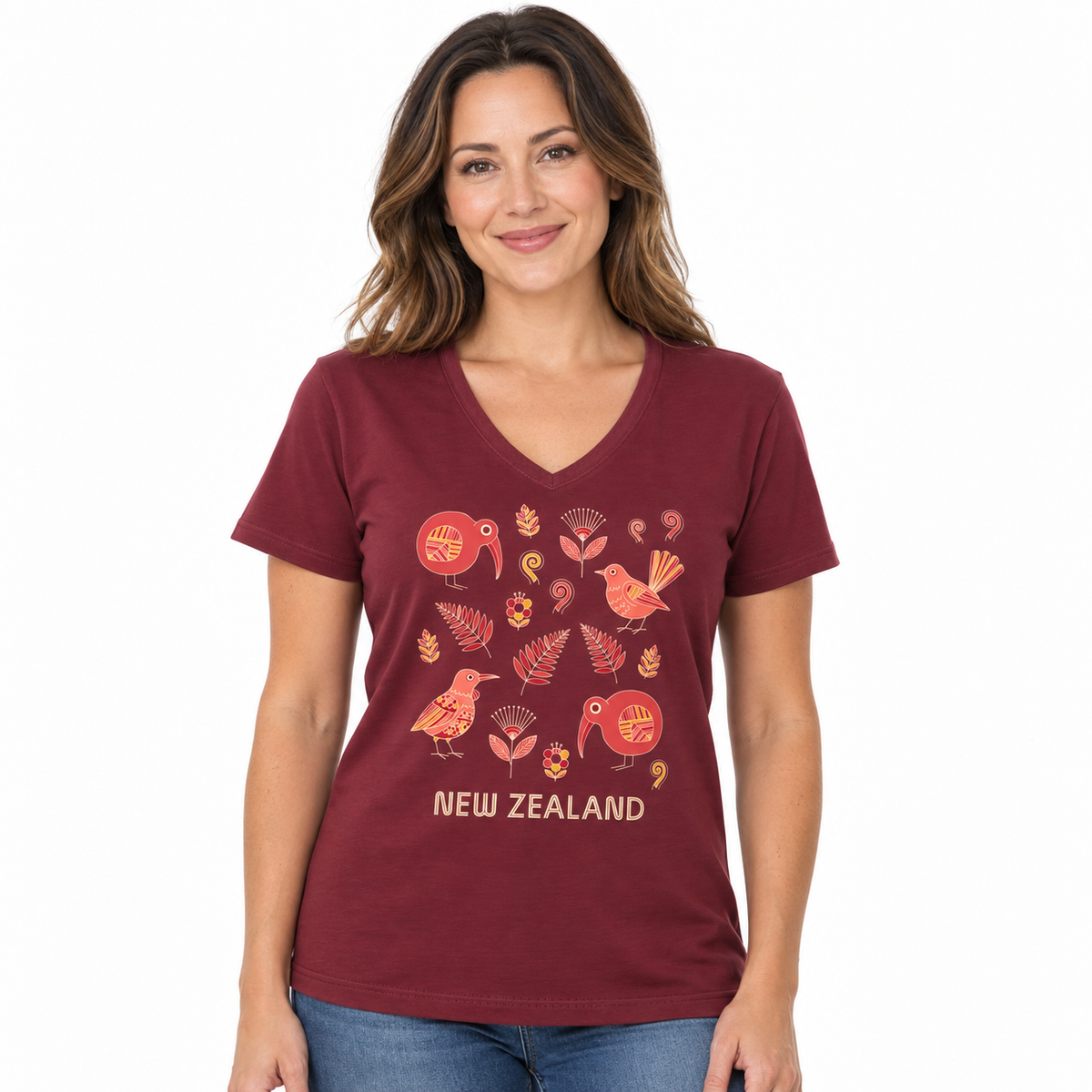 A woman wearing a maroon V-neck t-shirt with a New Zealand bird and leaf graphic print, paired with blue jeans, against a plain white background.