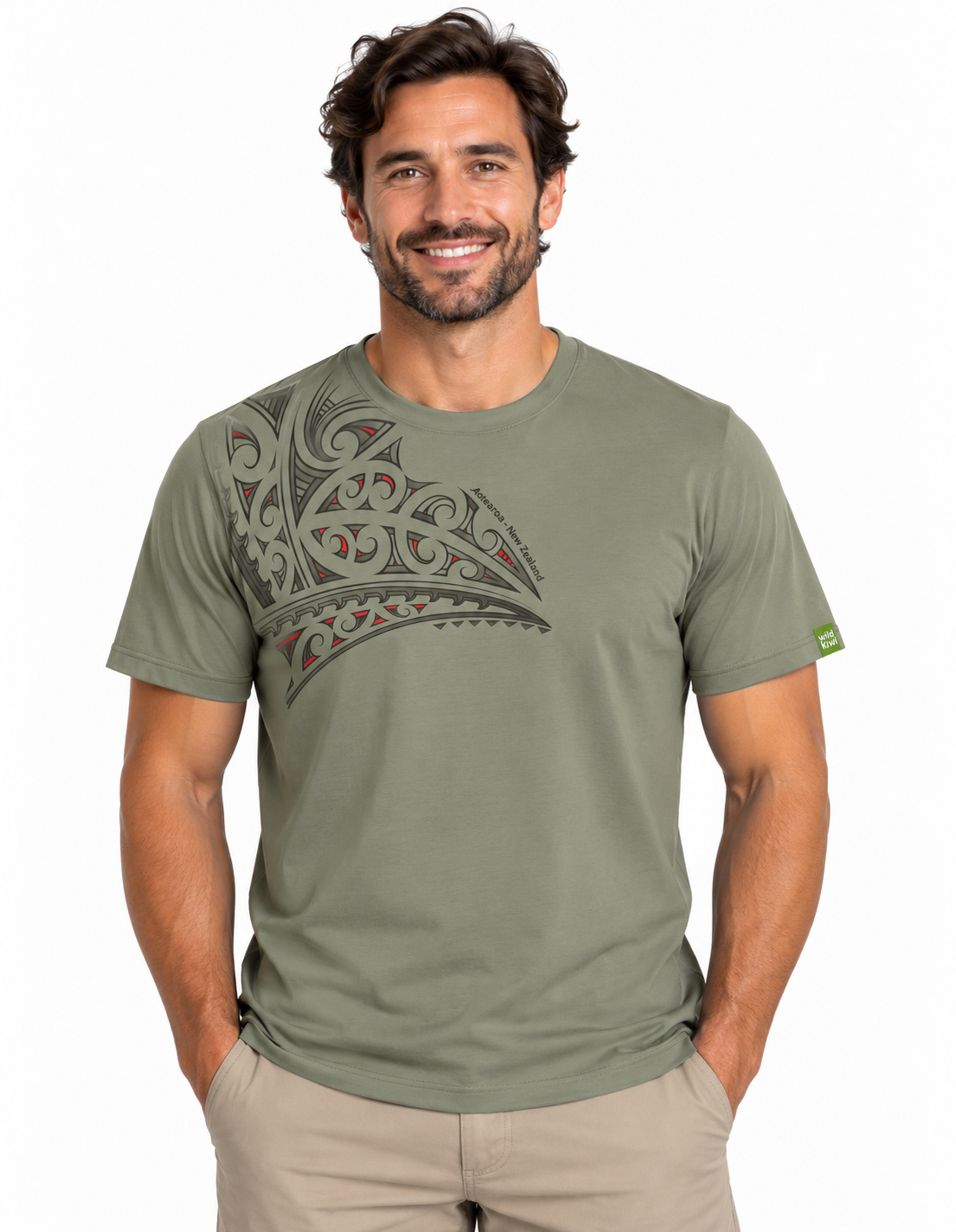 A man wearing an olive green crewneck t-shirt with a large Polynesian tribal graphic on the chest, paired with khaki pants, against a plain white background.