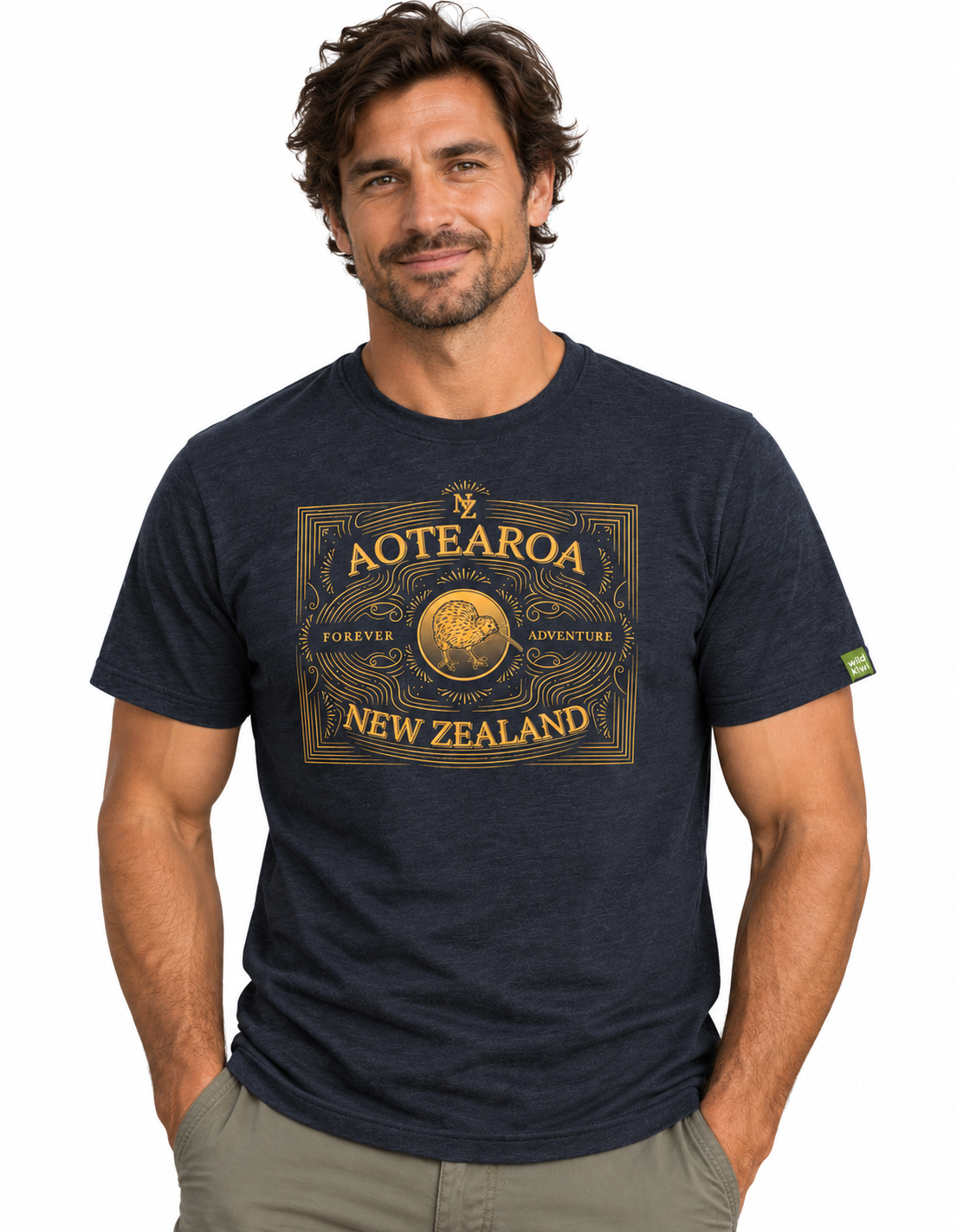 A man wearing a navy blue t-shirt with a large gold graphic on the front that reads 'AOTEOROA NEW ZEALAND', paired with khaki pants, against a plain white background.
