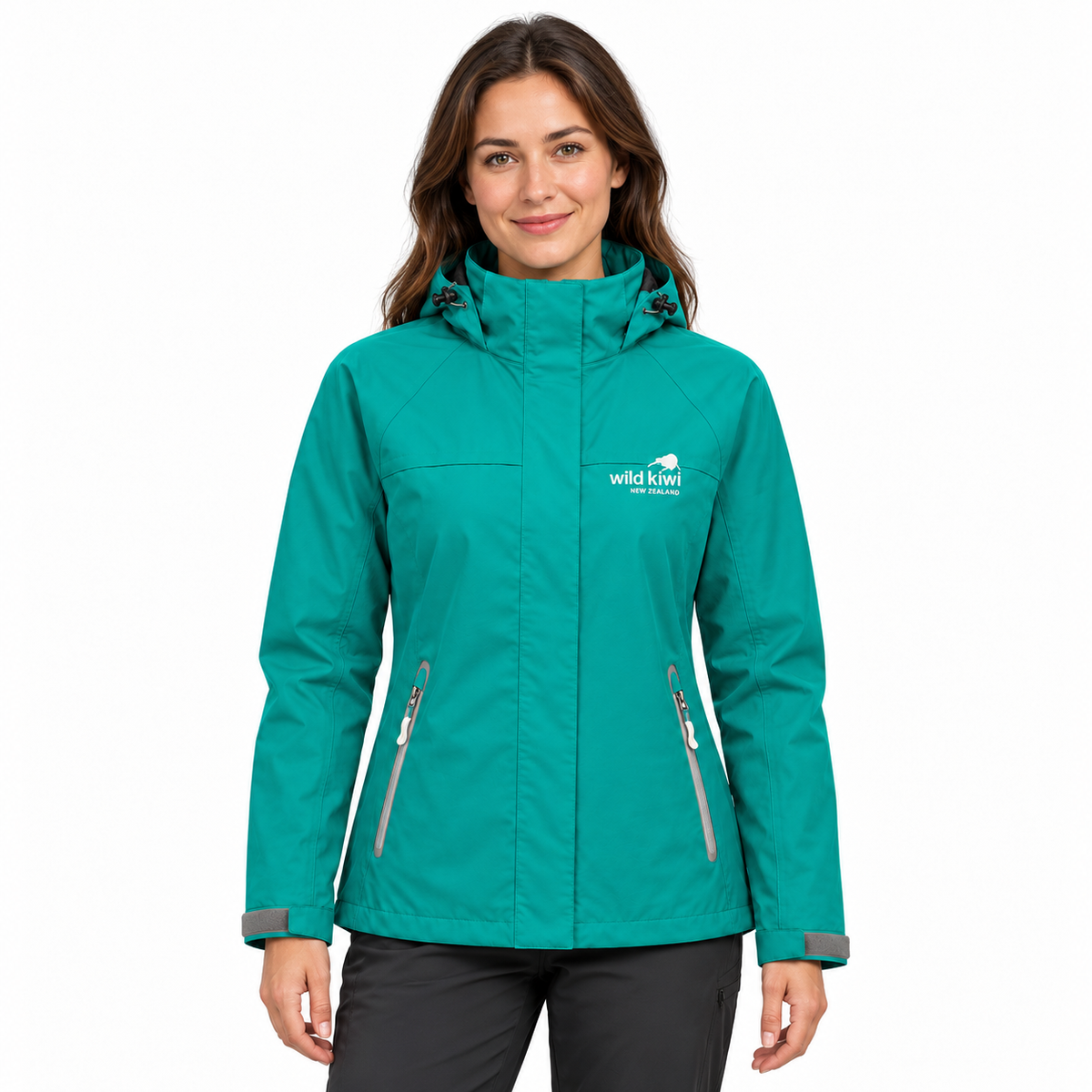 A woman wearing a teal green hooded outdoor jacket with gray zipper details and a white 'wild kiwi' logo on the left chest, paired with dark gray pants, against a plain white background.