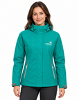 A woman wearing a teal green hooded outdoor jacket with gray zipper details and a white 'wild kiwi' logo on the left chest, paired with dark gray pants, against a plain white background.