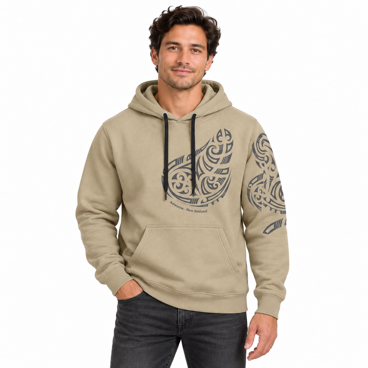 A man wearing a beige pullover hoodie with black graphic prints on the chest and sleeve, paired with dark gray jeans, against a plain white background.
