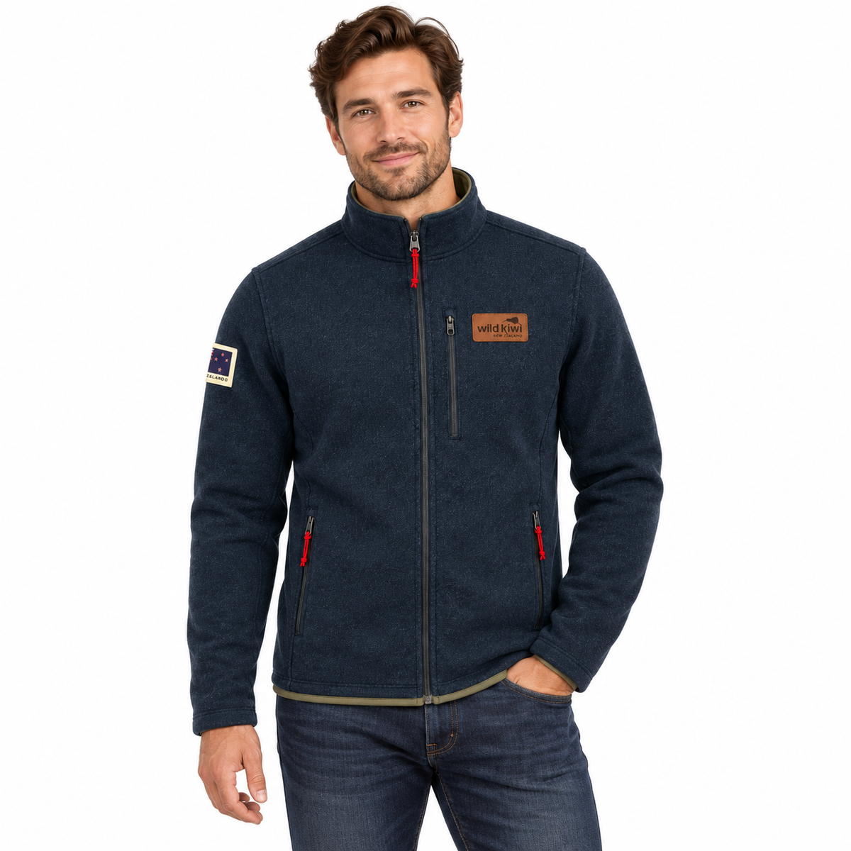 A man wearing a dark navy blue fleece jacket with a full-zip front, a brown brand patch on the chest, and red zipper pulls, paired with blue jeans against a plain white background.