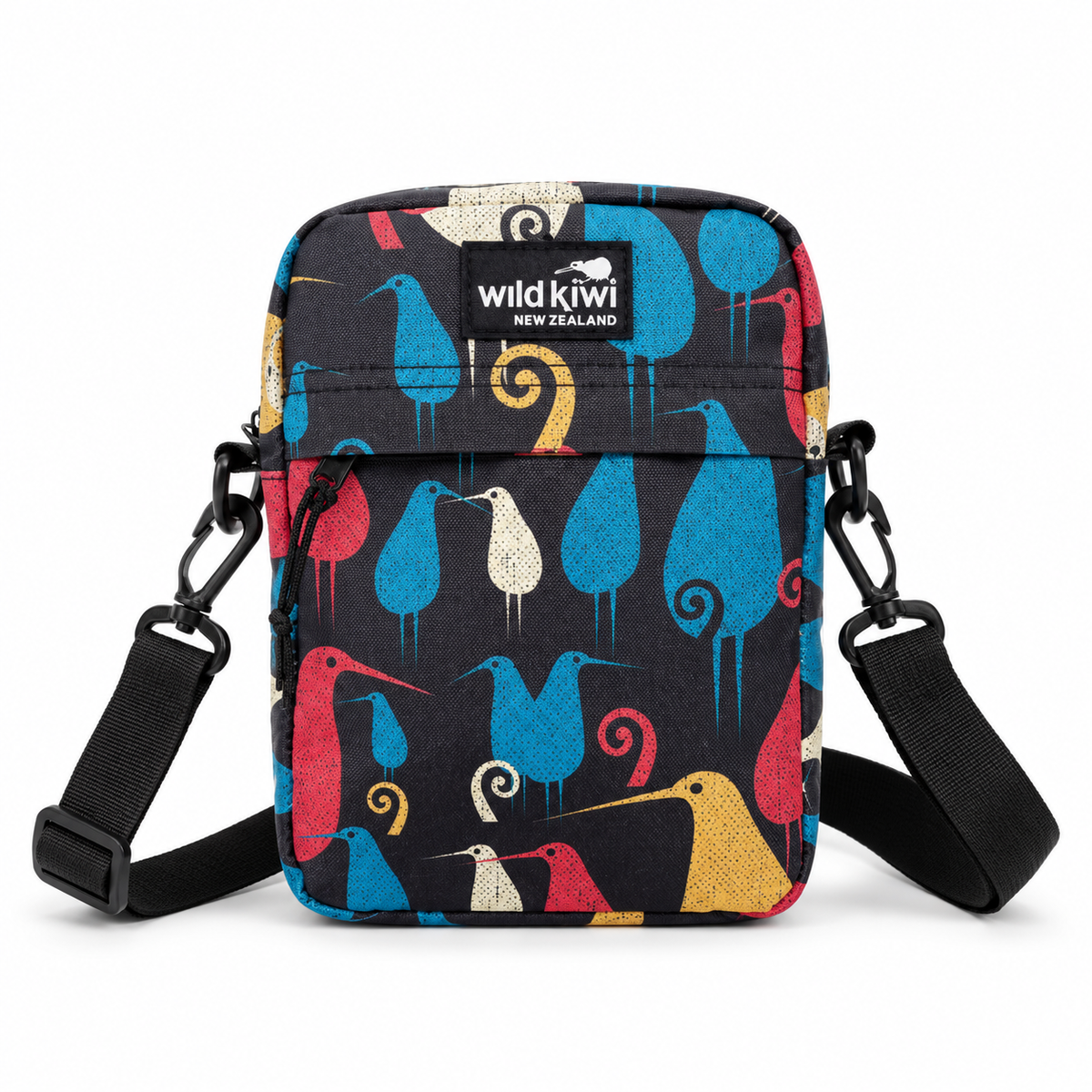 A small crossbody bag with a black background and a colourful bird pattern in blue, pink, yellow, and white. The bag features a black brand label reading 'wild kiwi New Zealand' and has an adjustable black shoulder strap with metal clips.