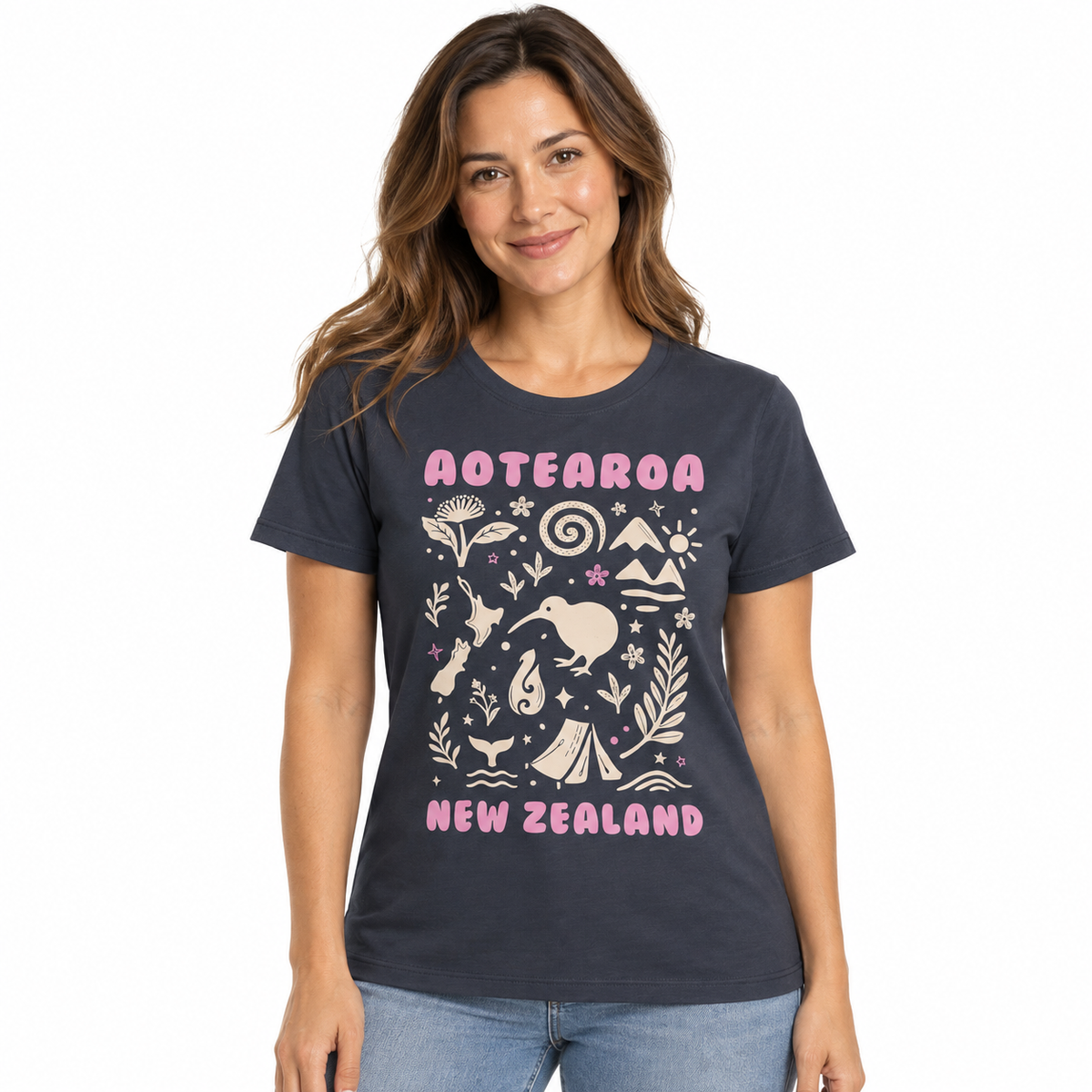A woman wearing a dark navy graphic t-shirt with 'AOTEAROA NEW ZEALAND' and New Zealand-themed illustrations in pink and cream, paired with light blue jeans, against a plain white background.
