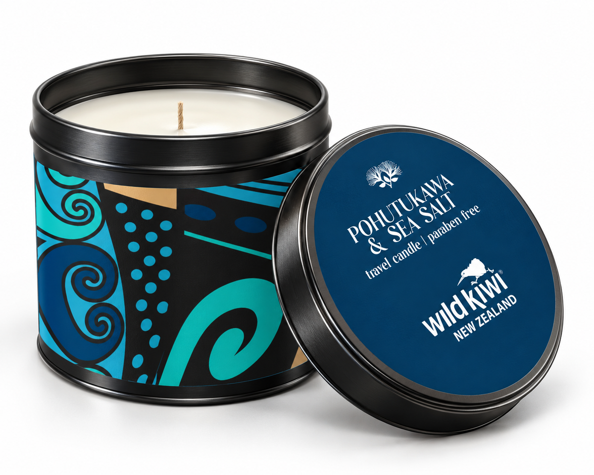 A tin candle shown open with the lid leaning beside it on a white studio background. The candle container has a black rim and a decorative label with blue, teal, black, and tan abstract patterns.