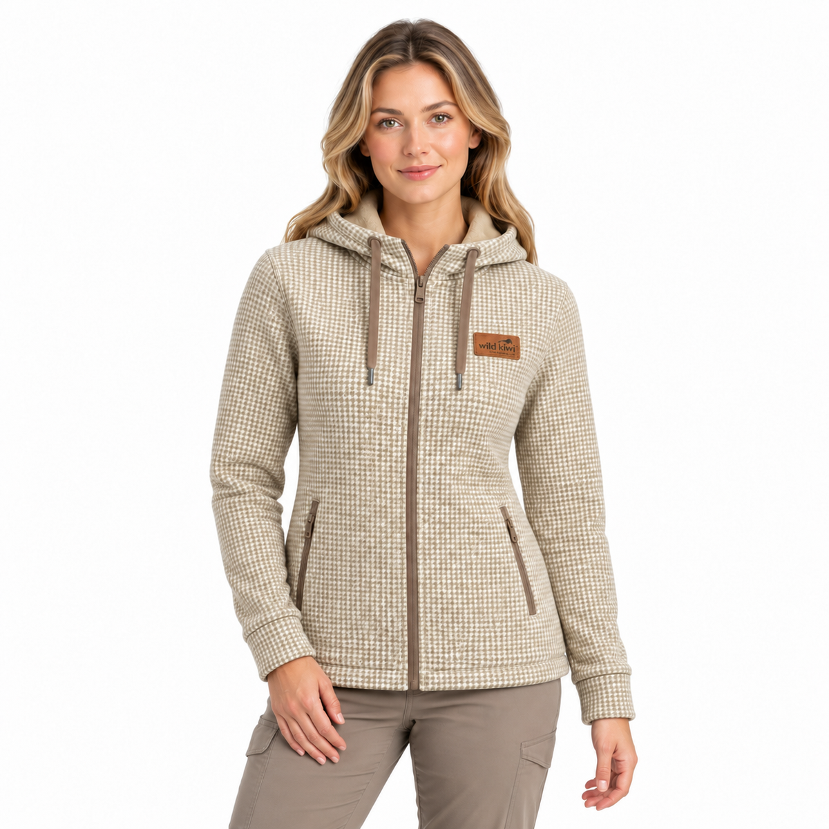 A woman modelling a beige and brown micro-check patterned zip-up hoodie with a drawstring hood, front pockets, and a small brown leather patch on the left chest, set against a plain white background.