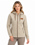 A woman modelling a beige and brown micro-check patterned zip-up hoodie with a drawstring hood, front pockets, and a small brown leather patch on the left chest, set against a plain white background.